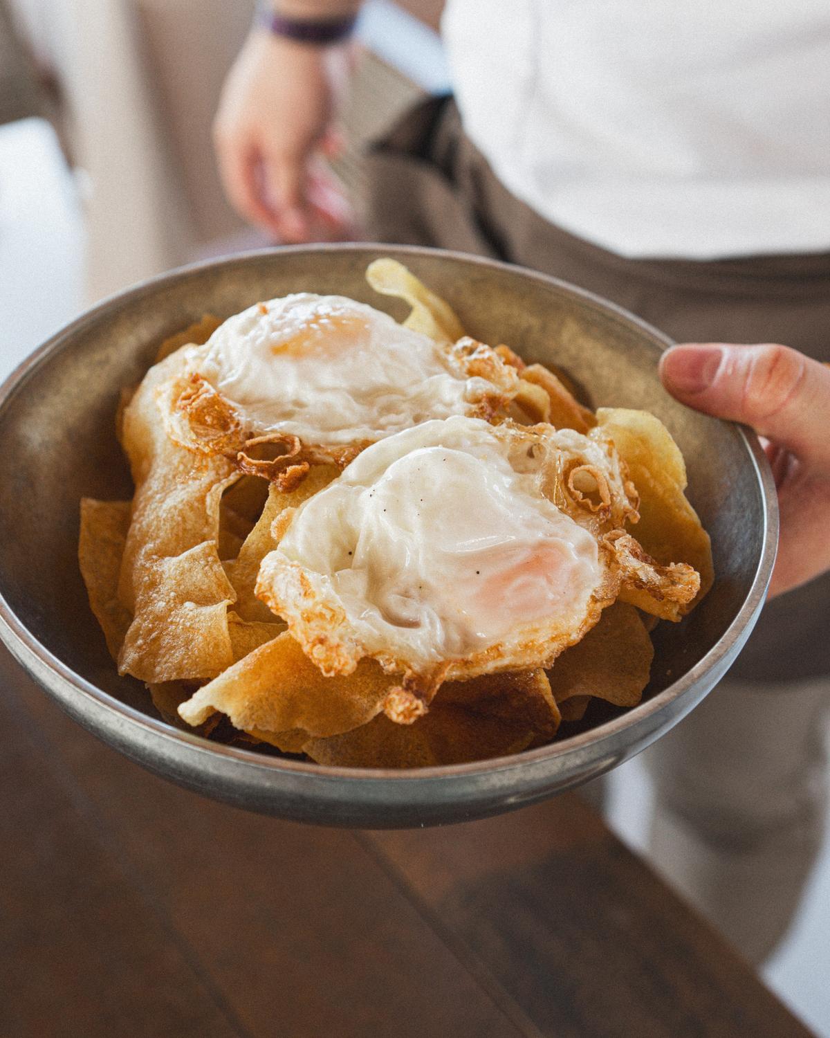 Huevos rotos sobre patatas servidos en cazo de metal