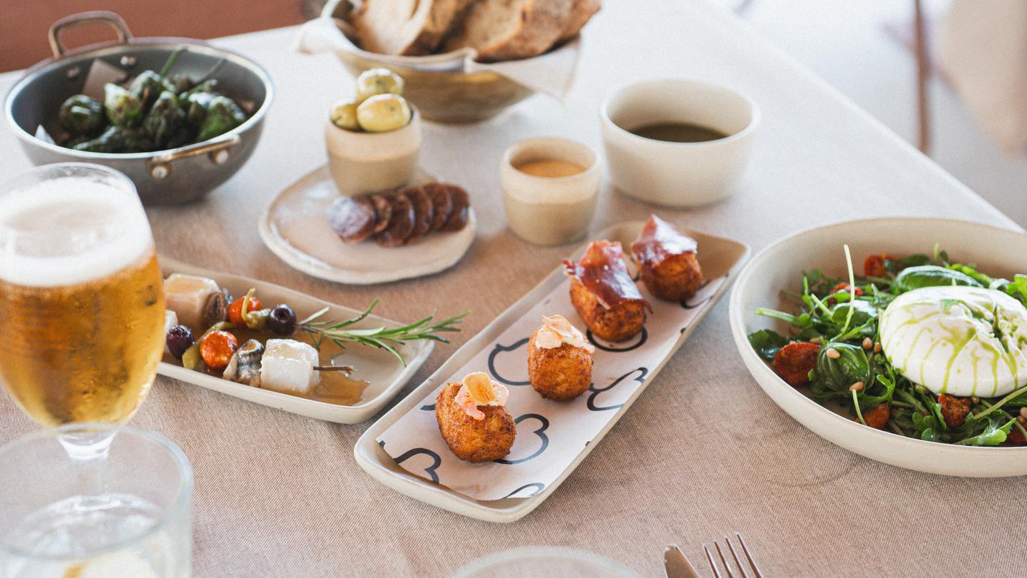 La mesa puesta de lado a lado: pan, mejillones, brochetas, croquetas y ensalada de burrata