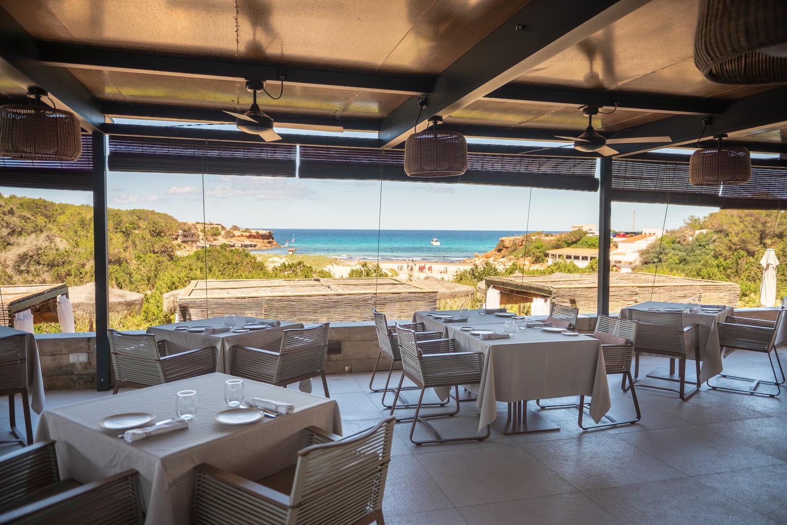 El comedor de Cala Saona con las mesas vestidas y la cala al fondo