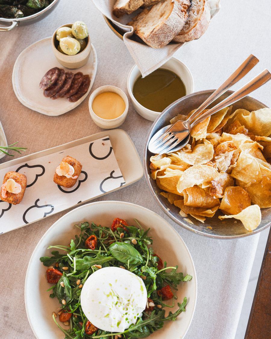 Mesa servida con ensalada de burrata, patatas, embutidos y pan para compartir